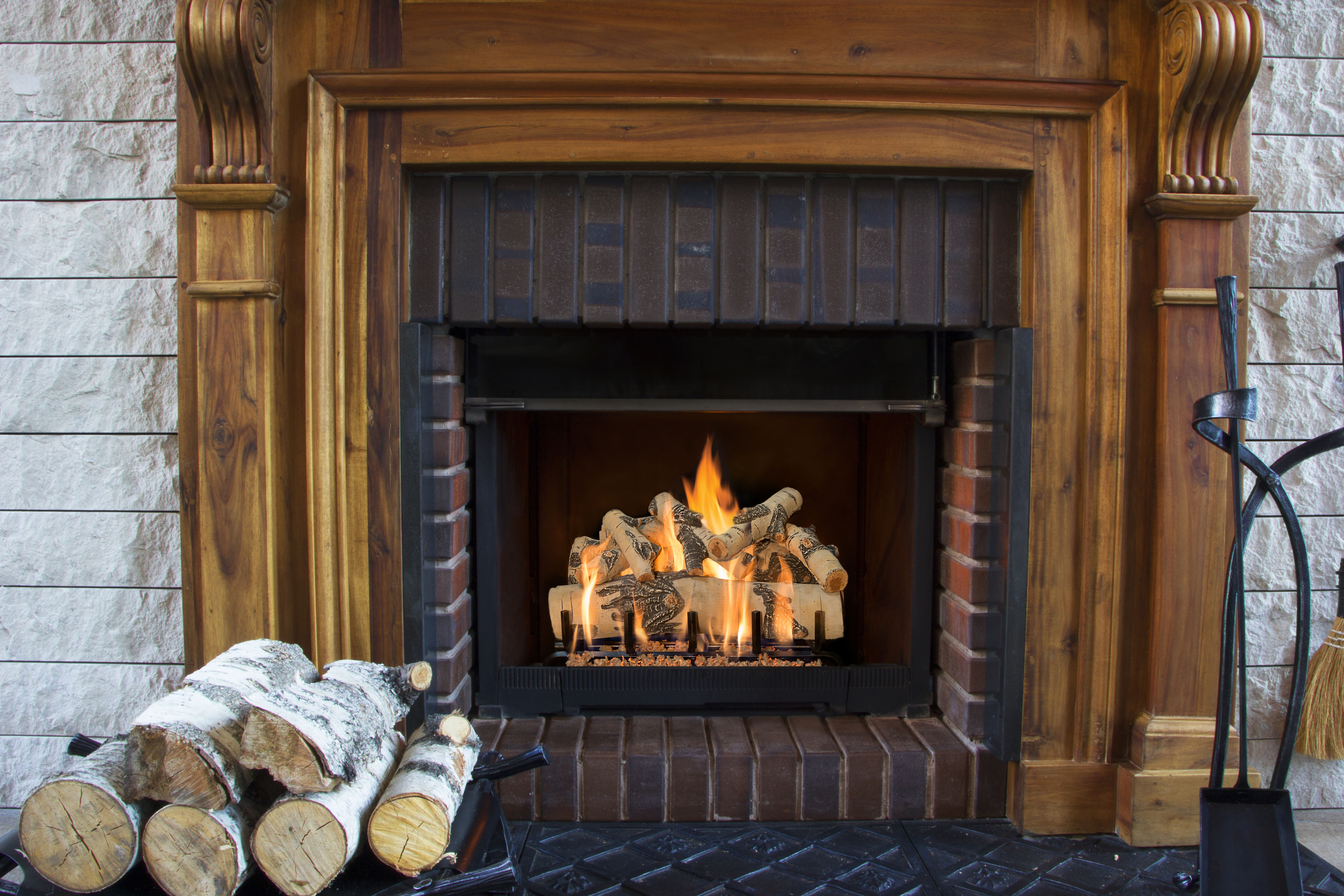 A traditional-looking, masonry hearth with a wooden mantel, a square fireplace, and a Birch wood gas log set.